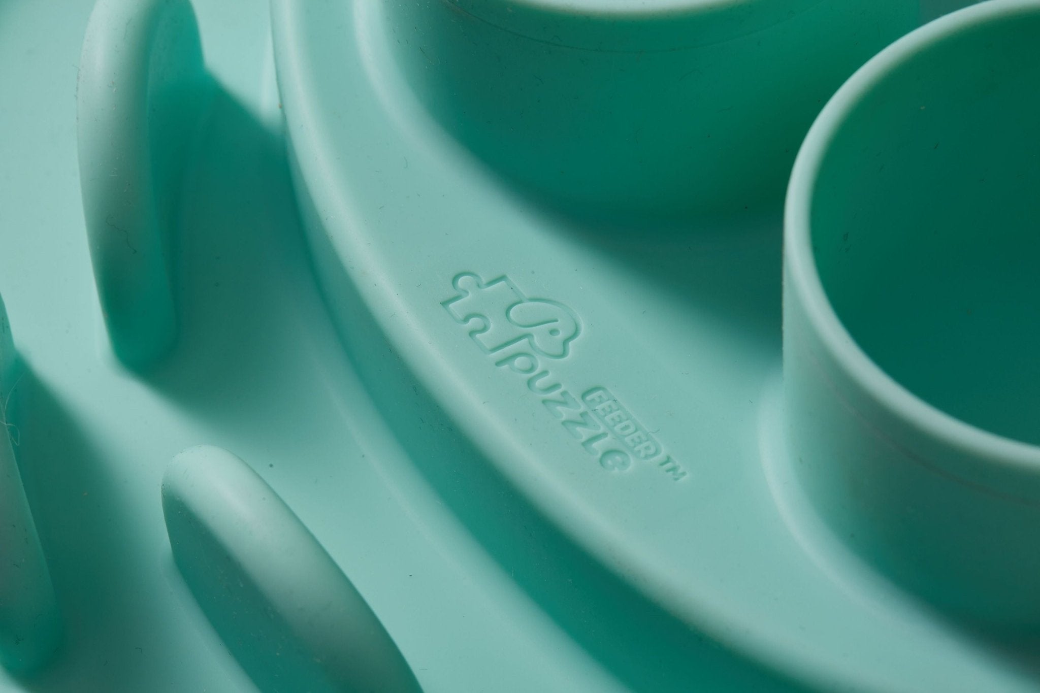 A detailed view of a textured, lawn-green plastic surface featuring raised sections and the words "Puzzle Digger" from Puzzle Feeder™, designed with non-toxic materials to stimulate your cat's hunting instinct.