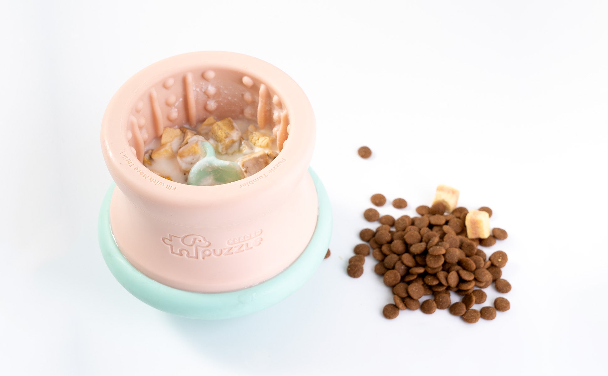 A pink and blue dog bowl puzzle feeder holds wet food, with kibble playfully scattered beside it.
