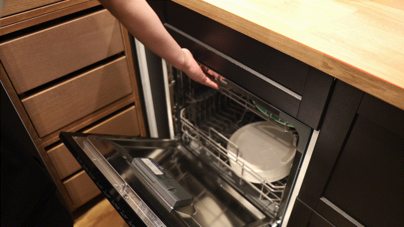 A hand loading a white plate into an open dishwasher in a modern kitchen, as if piecing together a puzzle, encourages you to slow down and savor daily routines.