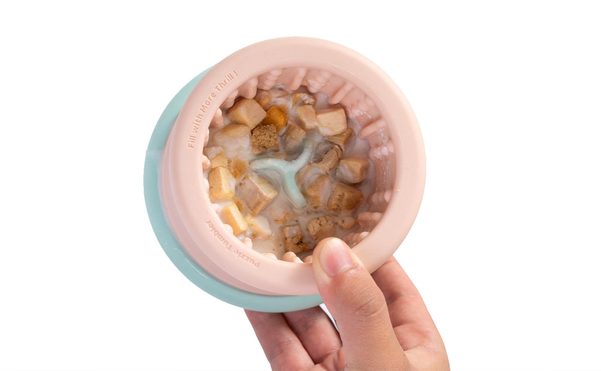 A hand holding a light pink dog bowl, designed as a slow feeder, showcases kibble pieces and water against a pristine white background.