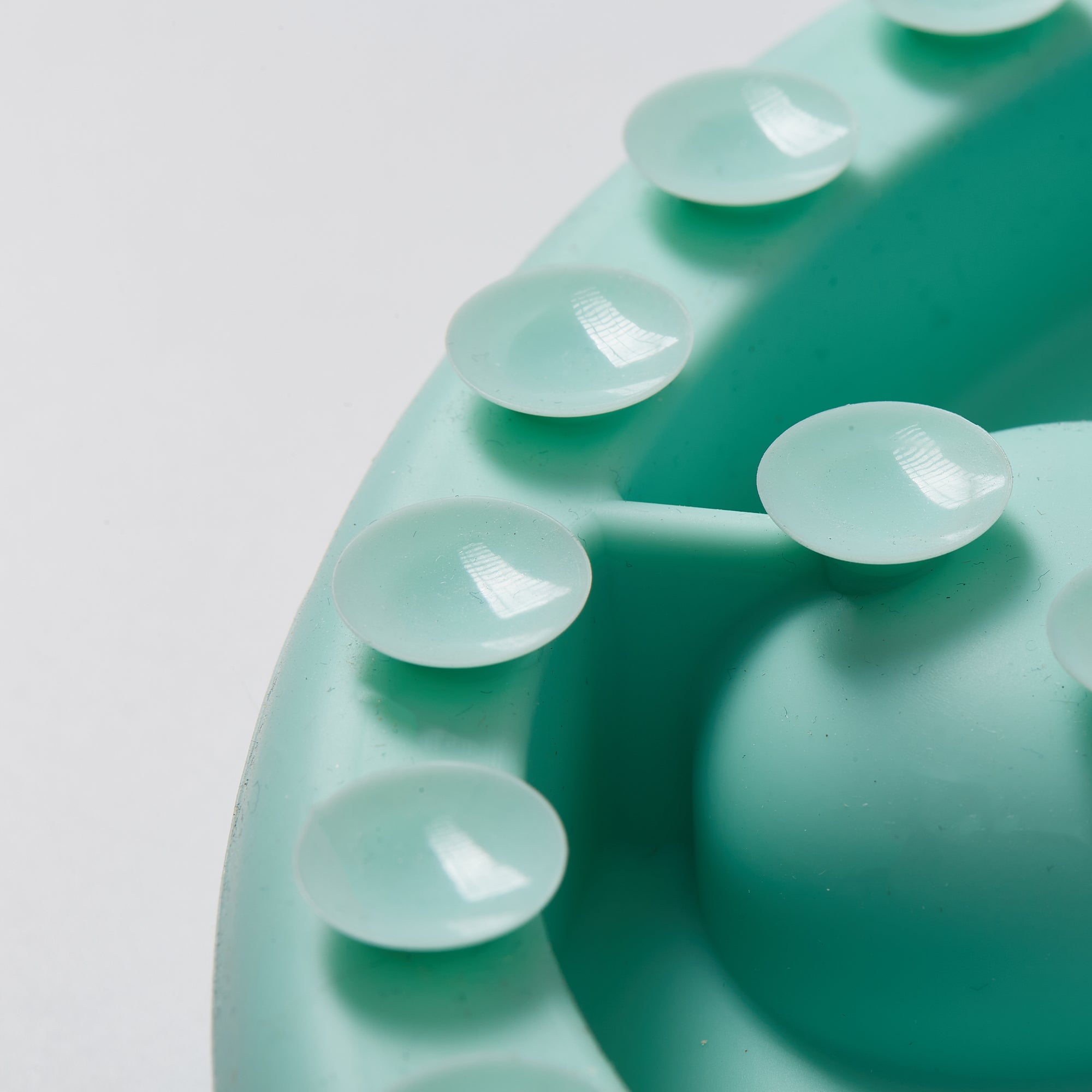 Close-up of a lawn-green plastic surface crafted from non-toxic materials, featuring rounded bumps arranged in a partial circle on a smooth background, inspired by biomimetic design. This is part of the Puzzle Digger - For Cat Hunting Instinct by Puzzle Feeder™.