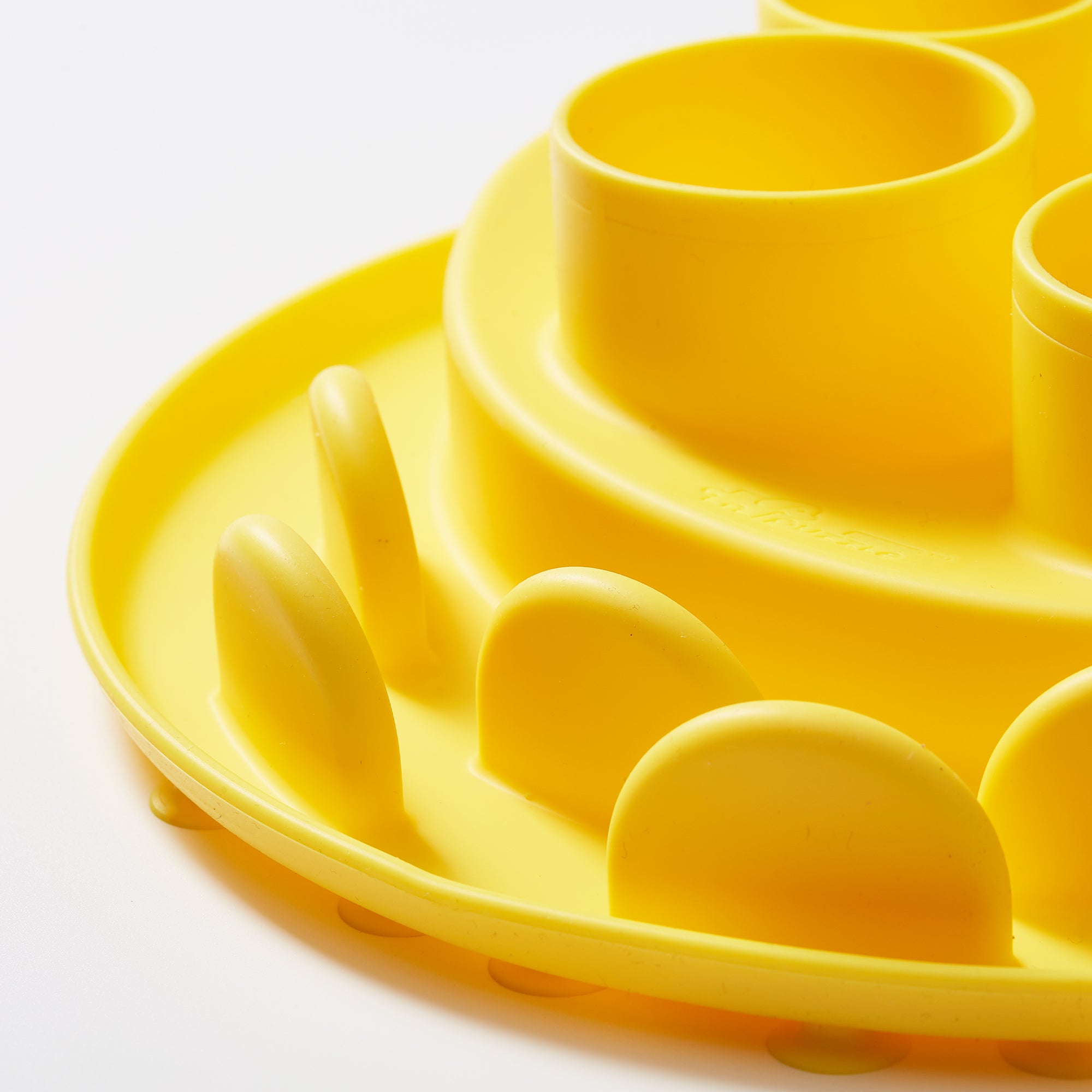 Close-up of the Wheat-Yellow Puzzle Digger by Puzzle Feeder™, a multi-level silicone mold with round compartments and a wavy edge, made from safe materials, set against a white background.