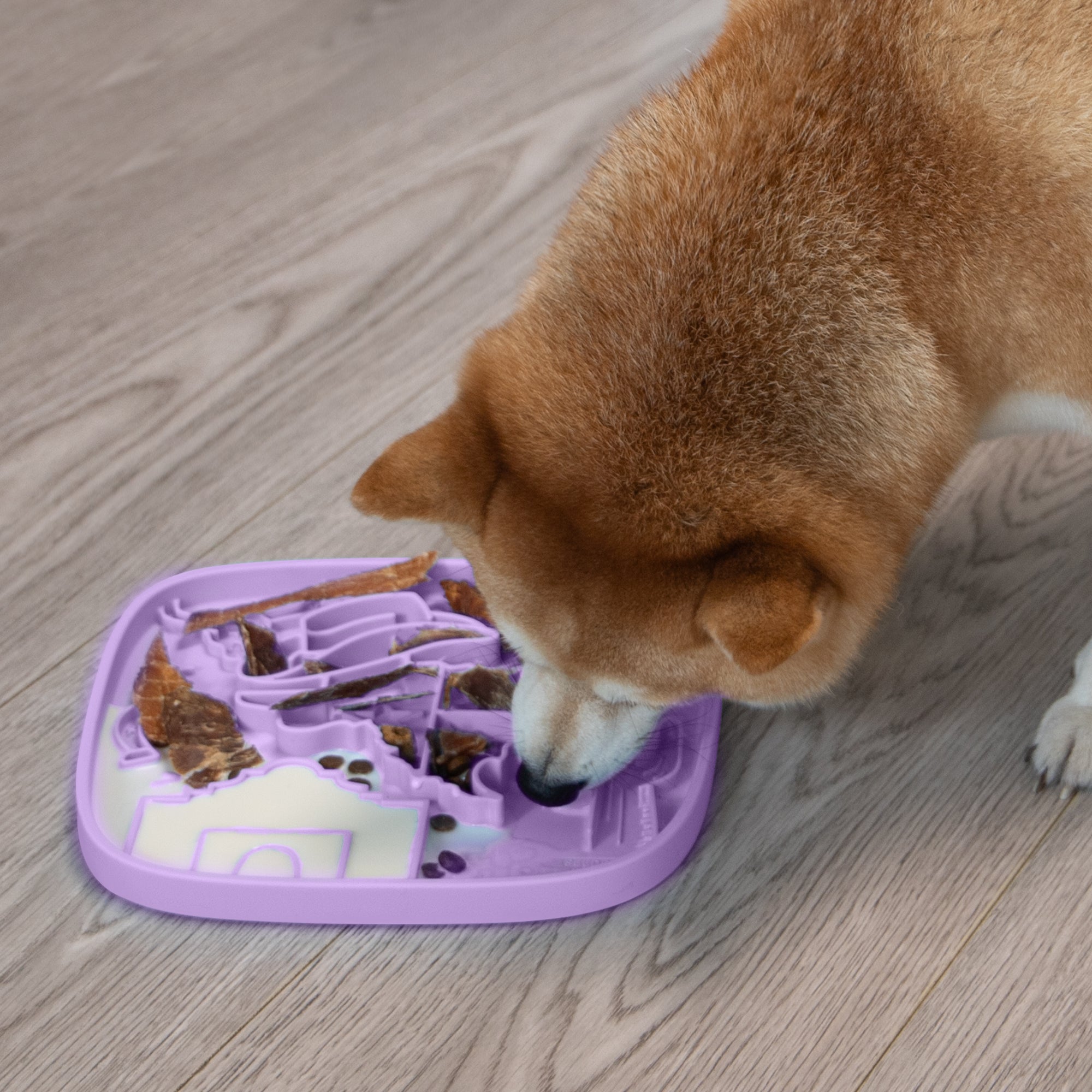 A dog relieves anxiety and stress while enjoying a meal from a Puzzle Feeder™ Texas Themed Lick Mat on a wooden floor.