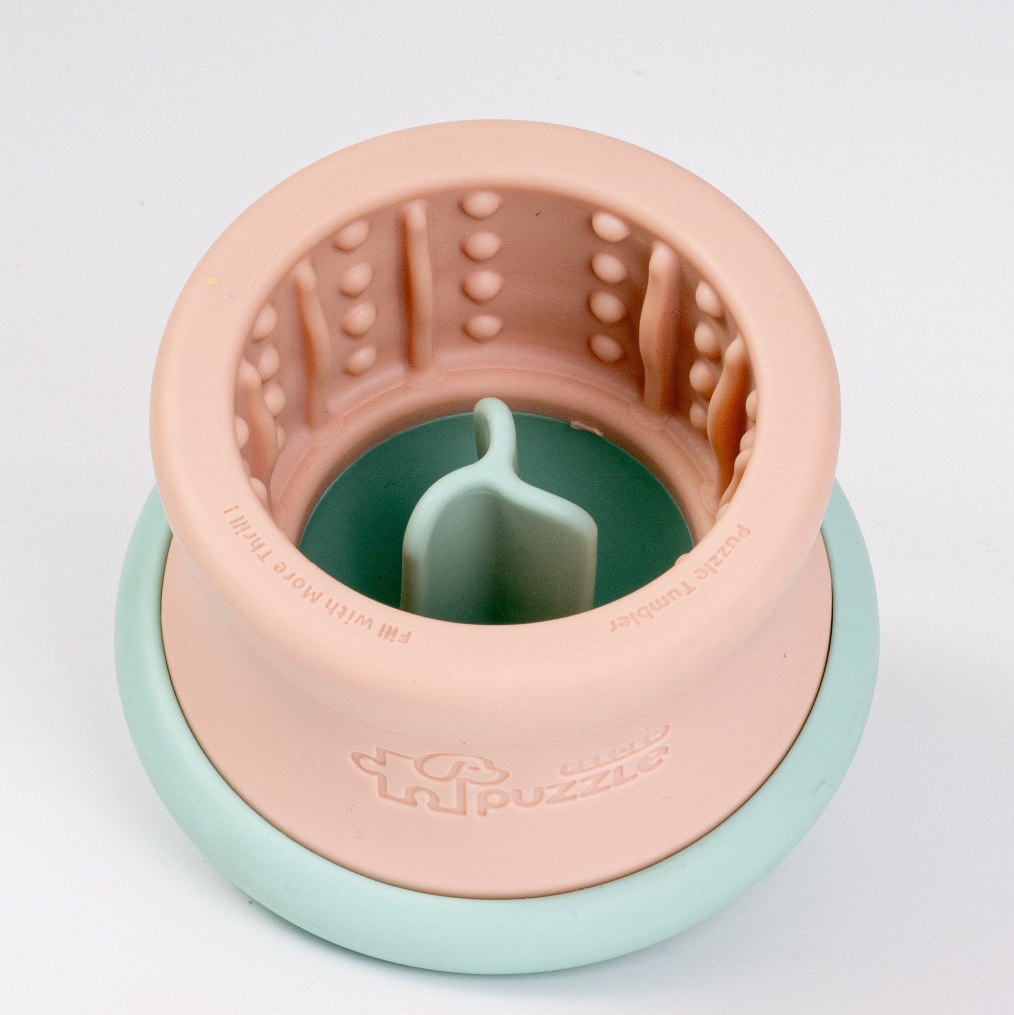 A pink and teal Dog Puzzle Tumbler, a cylindrical Puzzle Feeder Enrichment Toy designed for L/XL pups by Puzzle Feeder™, featuring a textured interior, handle, and the word "puzzle" embossed on one side, crafted from eco-friendly materials.