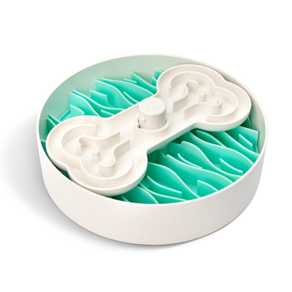 The Puzzle Feeder™ Swirl by Puzzle Feeder™ is a purple circular dog bowl with an elevated bone-shaped maze set atop teal, wave-like sections, designed to encourage healthy eating habits by making your pet’s mealtime slower.