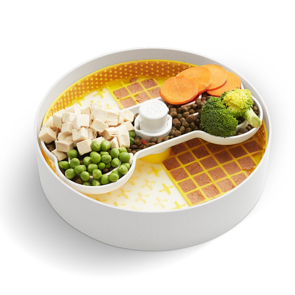 The Puzzle Licker Maze - Triple Textures, Triple Fun (Yellow) from Puzzle Feeder™ offers a creatively designed segmented dog feeder incorporating diced chicken, peas, kibble, sliced carrots, broccoli, and canned food on its yellow patterned base. This slow feeder dog bowl is engineered to promote healthy eating habits and support canine dental health through its thoughtful design.