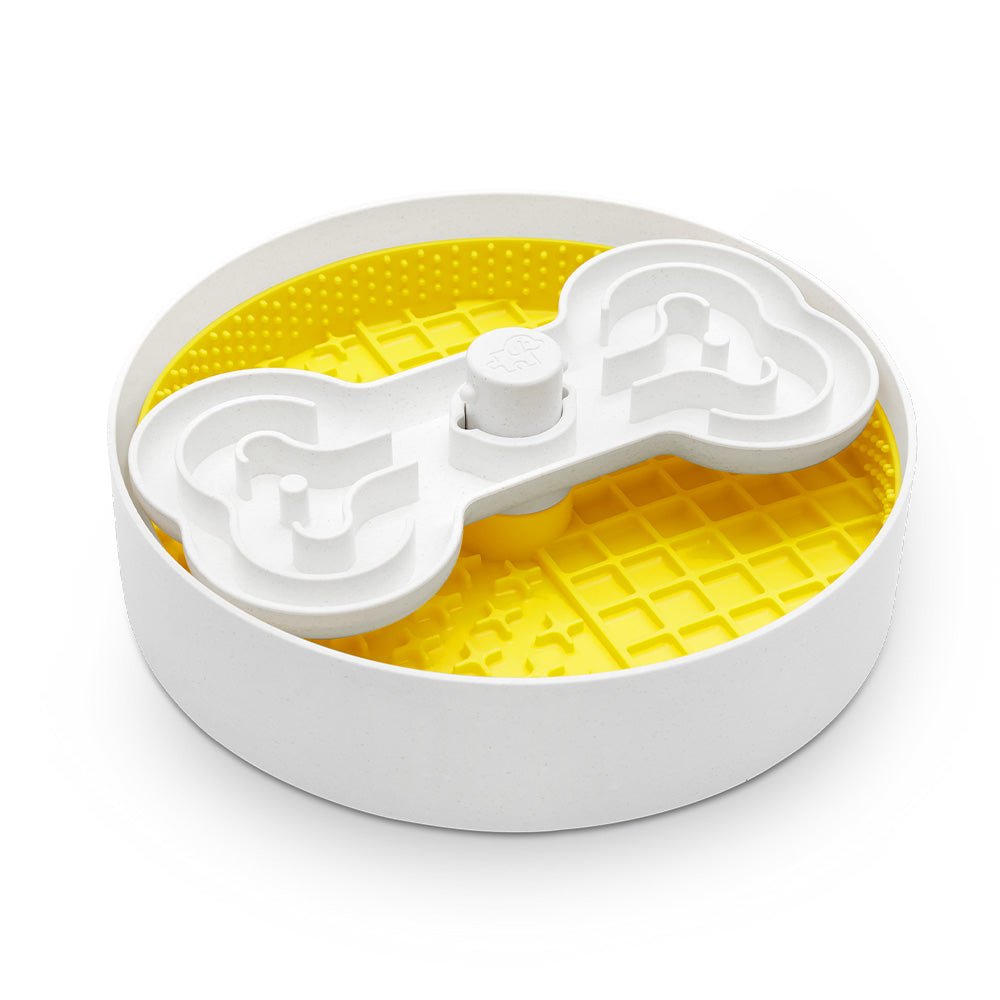 The Puzzle Licker Maze - Triple Textures, Triple Fun (Yellow) by Puzzle Feeder™ is a round puzzle feeder featuring a white bone-shaped top and a yellow grid-patterned interior, designed to entertain dogs while promoting dental health.