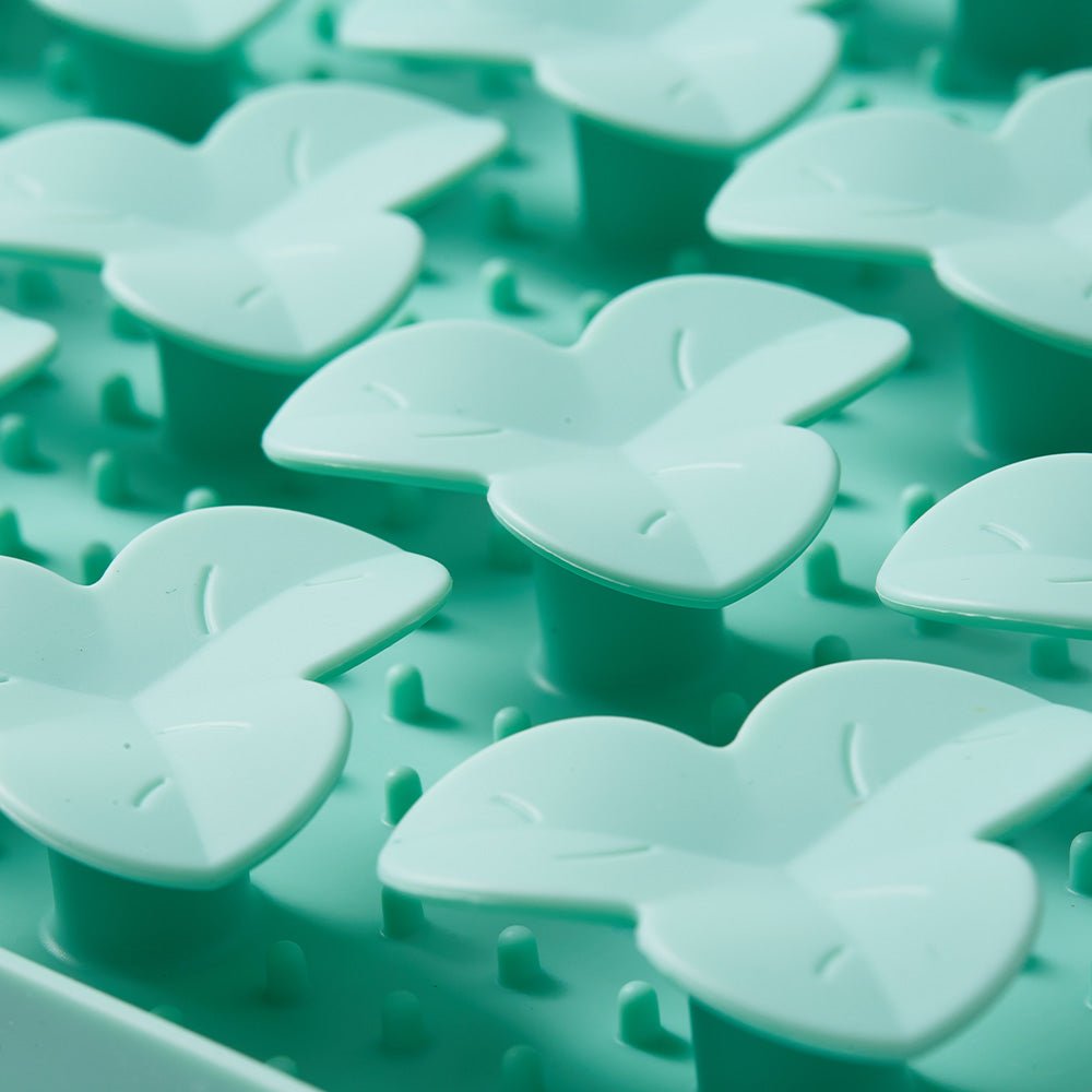 Close-up of green, butterfly-shaped pieces crafted from non-toxic materials on a textured surface, embodying biomimetic design. Part of the Dog Puzzle Mat - Slow Feeding Mat by Puzzle Feeder™.